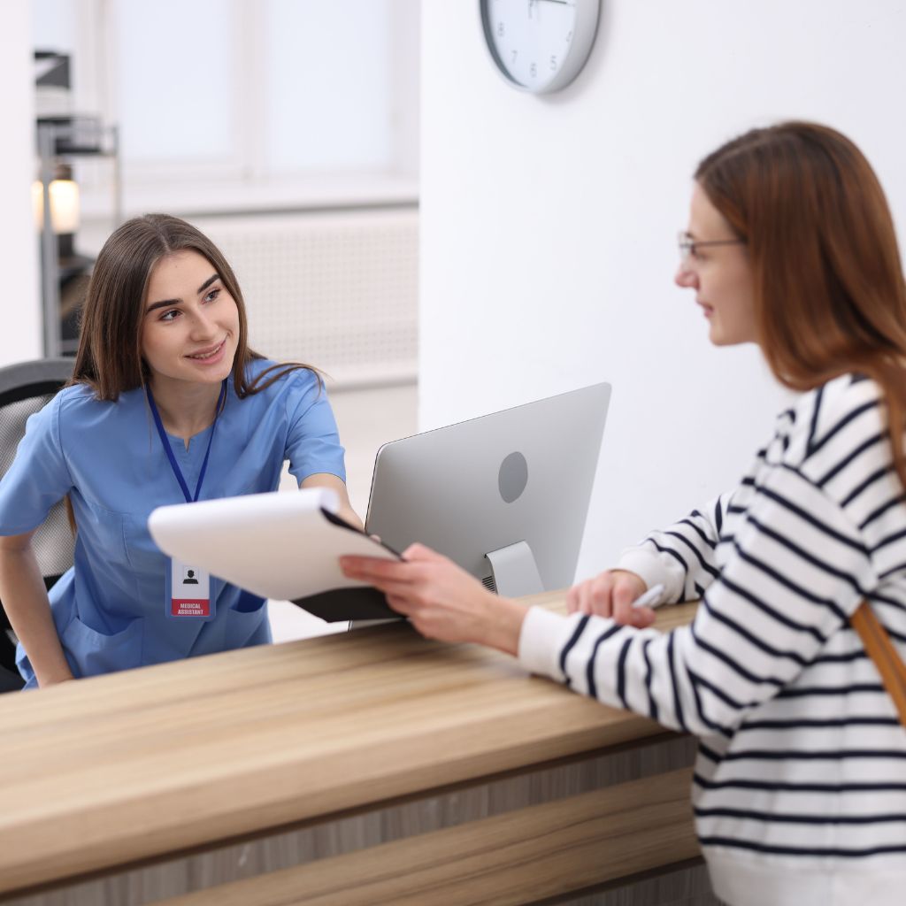 Healthcare staff member assisting a visitor at a reception desk
